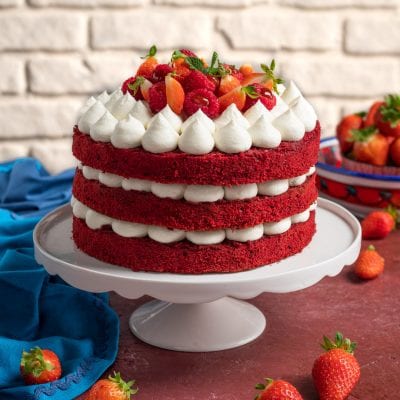 Red velvet a tre strati farcito con crema a ciuffi e guarnito con fragole e lamponi freschi