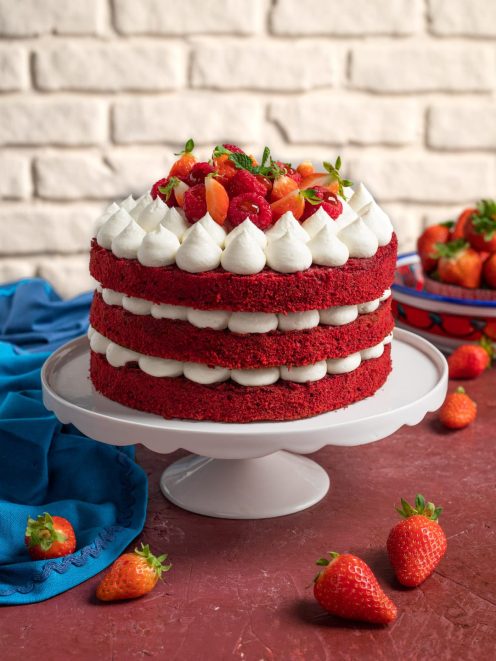 Red velvet a tre strati farcito con crema a ciuffi e guarnito con fragole e lamponi freschi