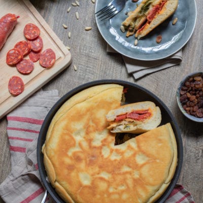 Focaccia tricolore in padella con una fetta sollevata che rivela il ripieno di salame e verdure