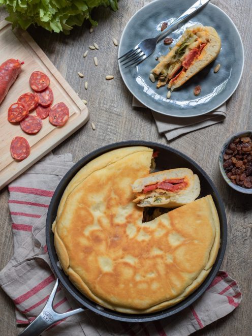 Focaccia tricolore in padella con una fetta sollevata che rivela il ripieno di salame e verdure