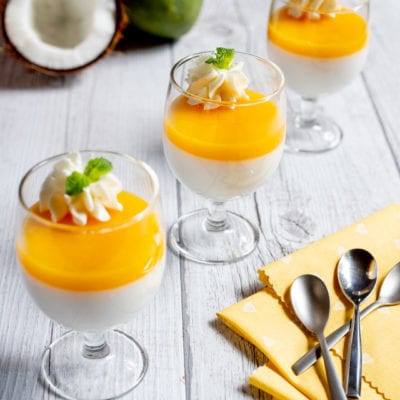 Dolce senza lattosio al cocco e mango servito in bicchieri con gelatina dorata e panna montata