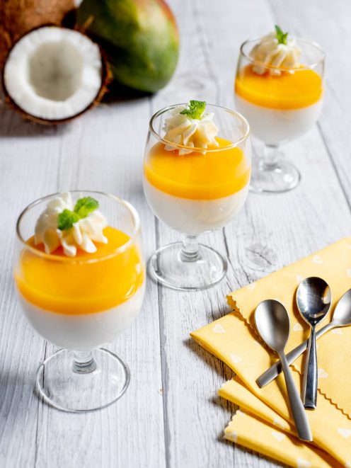 Dolce senza lattosio al cocco e mango servito in bicchieri con gelatina dorata e panna montata
