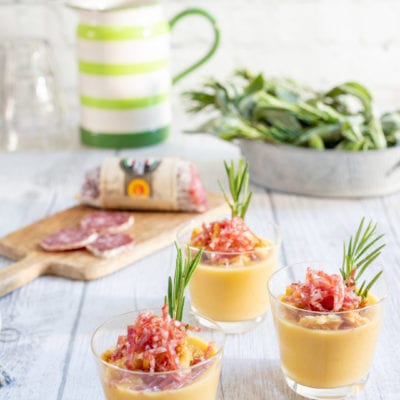 Crema di cannellini servita in bicchieri con crumble di pane, briciole di salame e un rametto di rosmarino