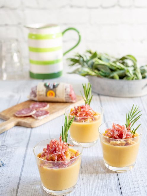 Crema di cannellini servita in bicchieri con crumble di pane, briciole di salame e un rametto di rosmarino