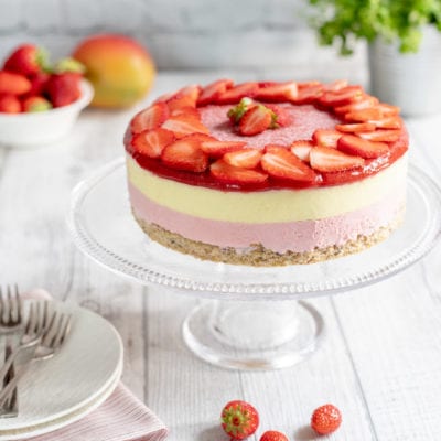 Mousse cake a strati con base di biscotto, mousse rosa e alla vaniglia, coronata da fragole fresche a fette