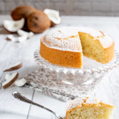 Torta al cocco spolverata di zucchero a velo, con una fetta servita in primo piano