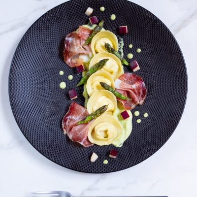 Cappellacci con ricotta su crema di asparagi, guarniti con speck, punte di asparago e cubetti di mela