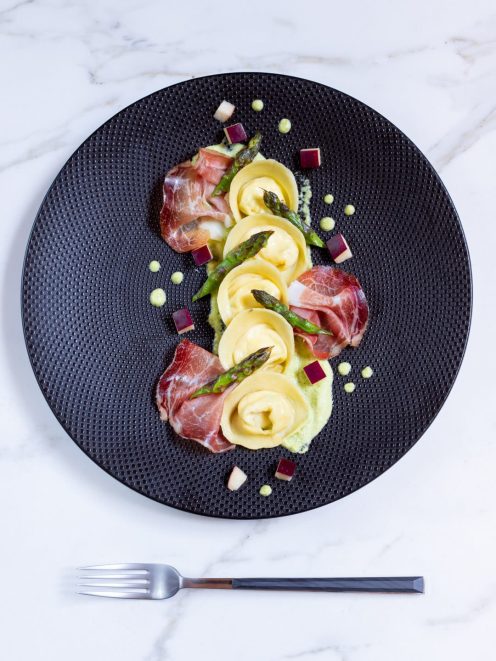Cappellacci con ricotta su crema di asparagi, guarniti con speck, punte di asparago e cubetti di mela