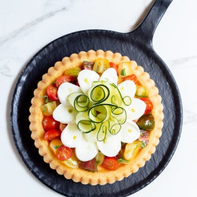 Crostata morbida con pomodorini colorati, fette di mozzarella e riccioli di zucchina con gocce di pesto