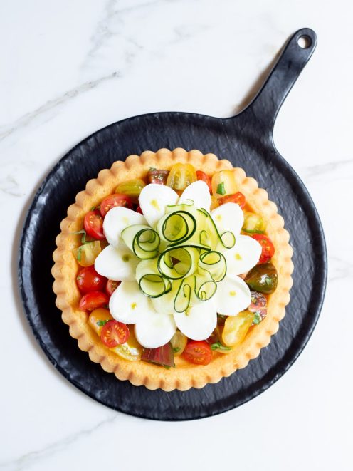 Crostata morbida con pomodorini colorati, fette di mozzarella e riccioli di zucchina con gocce di pesto