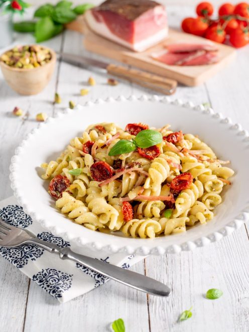 Pasta con pesto di pistacchi, speck e pomodorini confit con foglie di basilico fresco