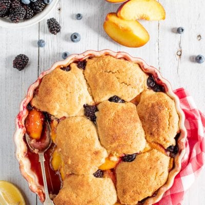 Cobbler con pesche e frutti di bosco, coperto da biscotti dorati e croccanti appena sfornati