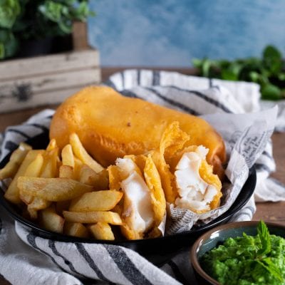 Fish and chips con mushy peas: filetto in pastella dorata aperto, patatine fritte e purè di piselli