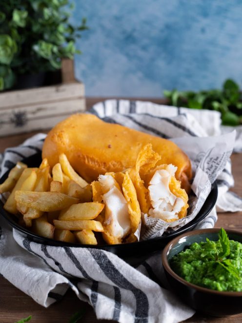 Fish and chips con mushy peas: filetto in pastella dorata aperto, patatine fritte e purè di piselli