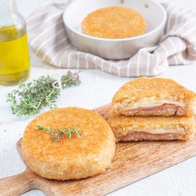 Supplì di riso dorati e panati, uno tagliato a metà con ripieno di mozzarella filante e salume