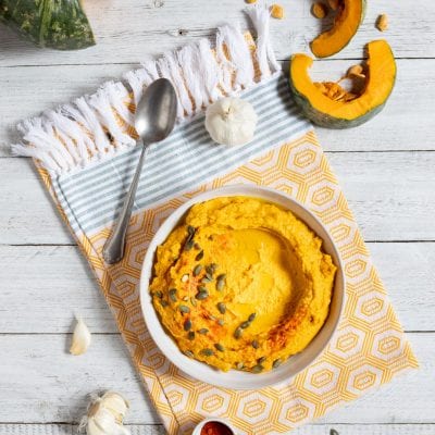 Hummus di zucca guarnito con semi di zucca e paprika, servito con zucca fresca e aglio