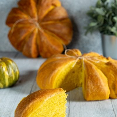 Pane di zucca a forma di zucca legato con spago, con una fetta dal cuore giallo intenso in primo piano