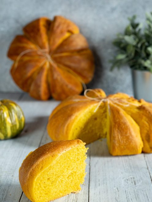 Pane di zucca a forma di zucca legato con spago, con una fetta dal cuore giallo intenso in primo piano
