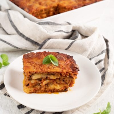 Parmigiana di melanzane con strati di sugo, mozzarella e riso, guarnita con foglie di basilico fresco
