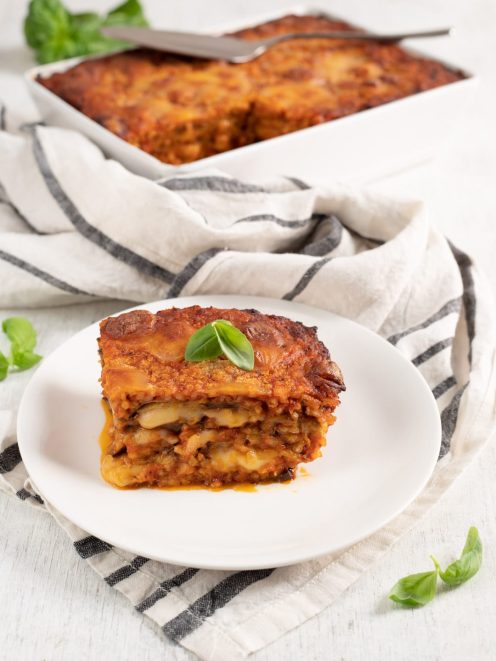 Parmigiana di melanzane con strati di sugo, mozzarella e riso, guarnita con foglie di basilico fresco