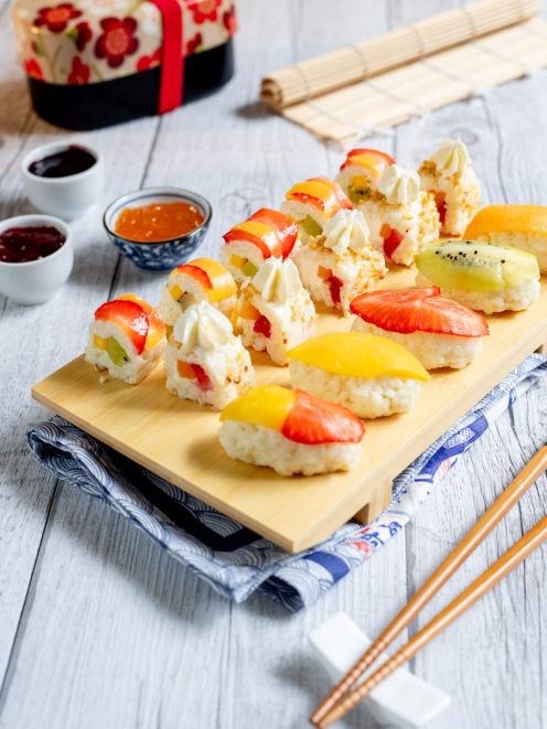 Sushi di frutta con fragole, mango, kiwi e ciuffi di panna su base di riso dolce