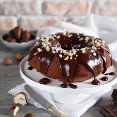 Ciambella di castagne con glassa al cioccolato colante e granella di nocciole in superficie