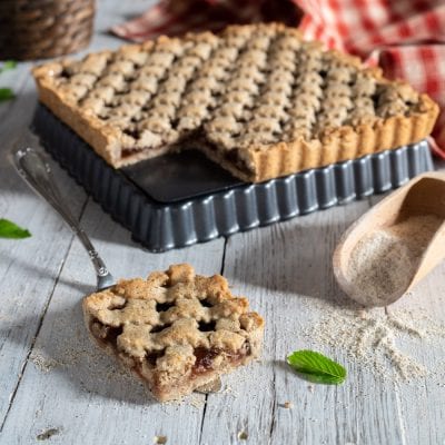 Crostata di grano saraceno con reticolo decorato e una fetta servita che rivela il ripieno di marmellata