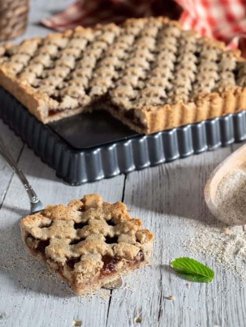 Crostata di grano saraceno con reticolo decorato e una fetta servita che rivela il ripieno di marmellata
