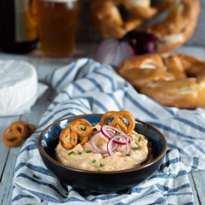 Obatzda cremoso guarnito con rondelle di cipolla rossa, erba cipollina e bretzel piccoli