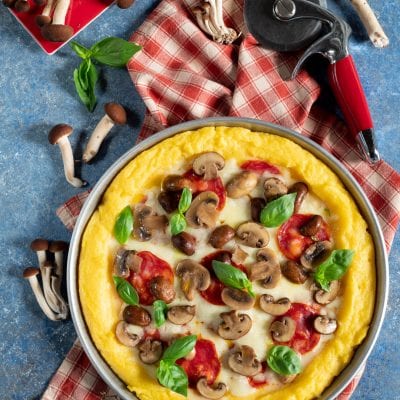 Pizza di polenta con funghi champignon, salsa di pomodoro, mozzarella filante e foglie di basilico fresco