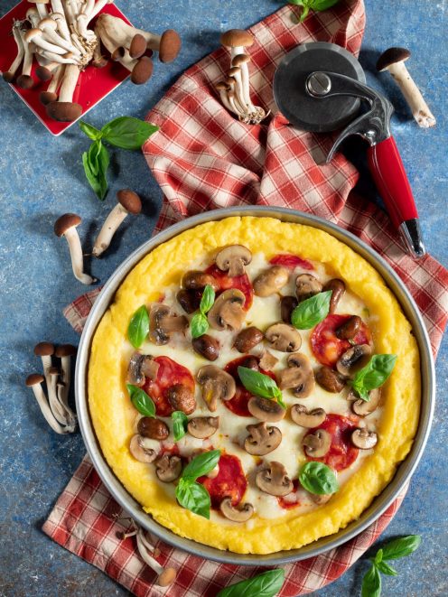 Pizza di polenta con funghi champignon, salsa di pomodoro, mozzarella filante e foglie di basilico fresco