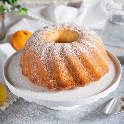 Ciambella all'acqua dorata con superficie striata, spolverata di zucchero a velo su alzata bianca