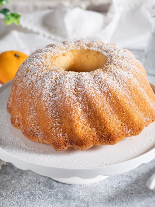Ciambella all'acqua dorata con superficie striata, spolverata di zucchero a velo su alzata bianca