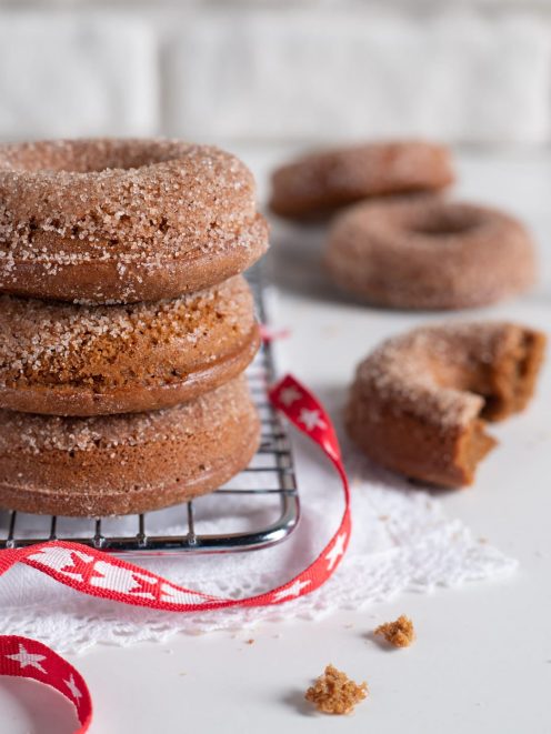 Gingerbread donuts impilati su griglia, ricoperti di zucchero granulato, con uno spezzato accanto