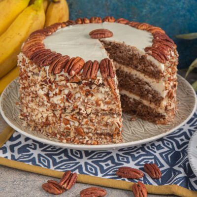 Hummingbird cake a strati con crema al formaggio, rivestita di noci pecan tritate e decorata con pecan interi sul bordo