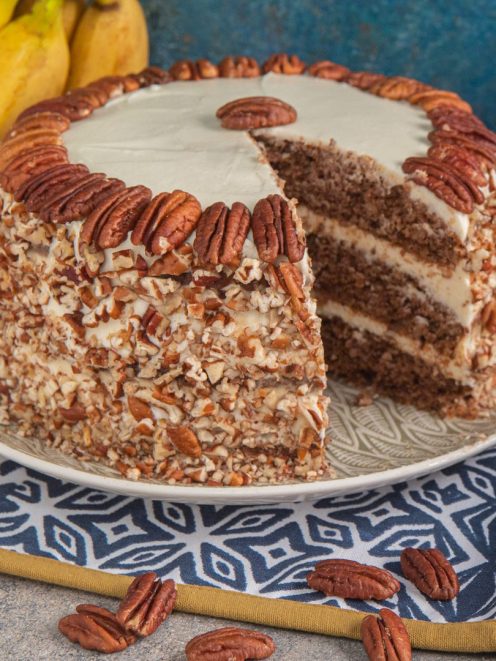 Hummingbird cake a strati con crema al formaggio, rivestita di noci pecan tritate e decorata con pecan interi sul bordo