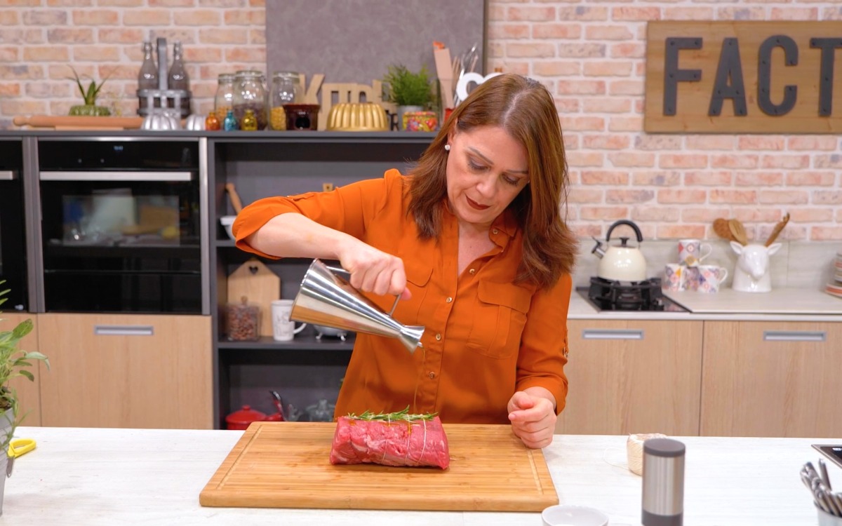 Olio versato su un pezzo di carne legato con spago e rametti di rosmarino sul tagliere