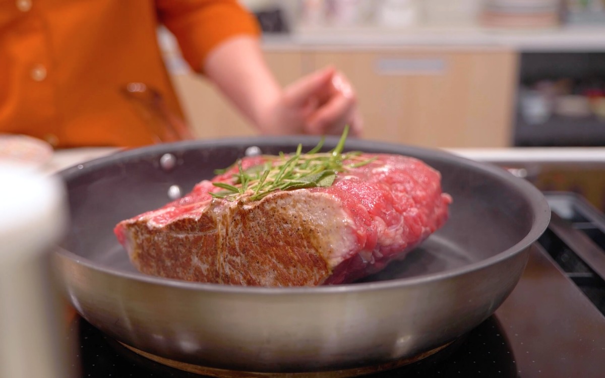 Pezzo di roast beef che rosola in padella con un rametto di rosmarino sopra