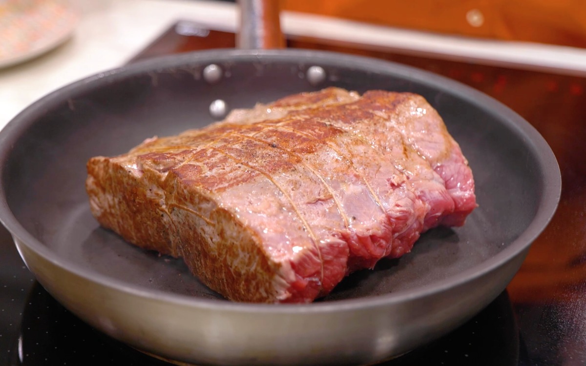 Pezzo di roast beef legato con spago rosolato su un lato in padella
