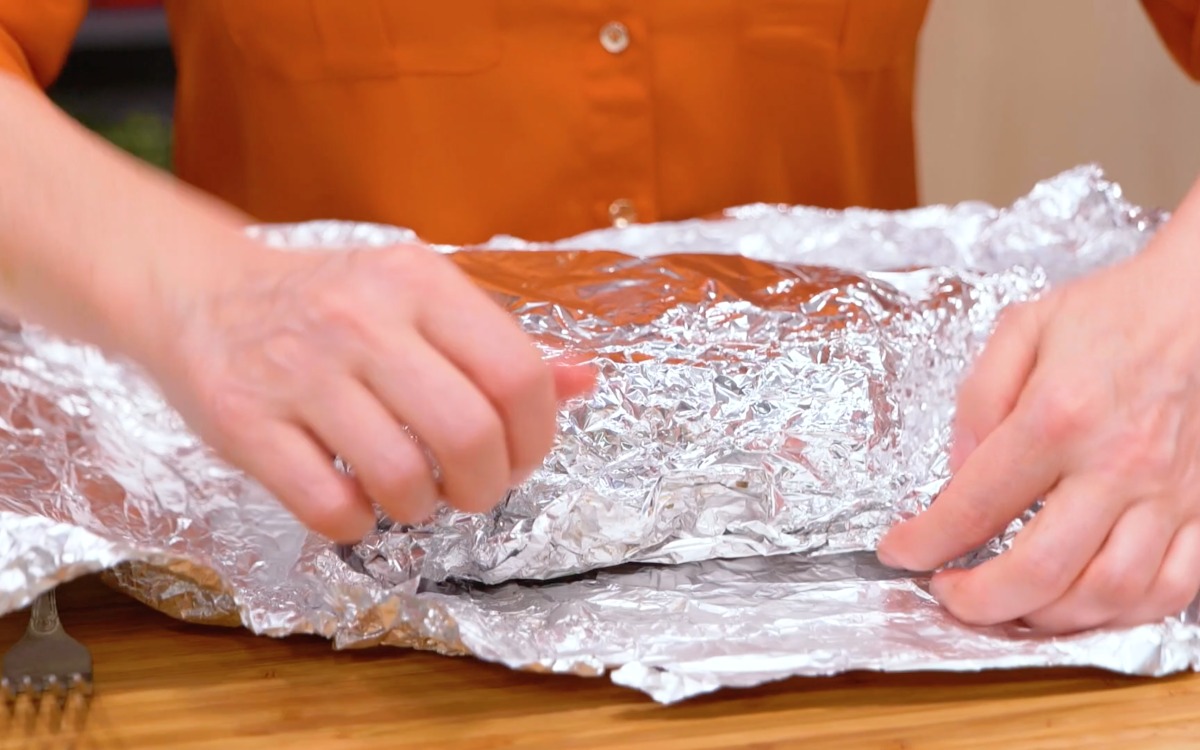 Mani che avvolgono il roast beef in un foglio di alluminio per il riposo