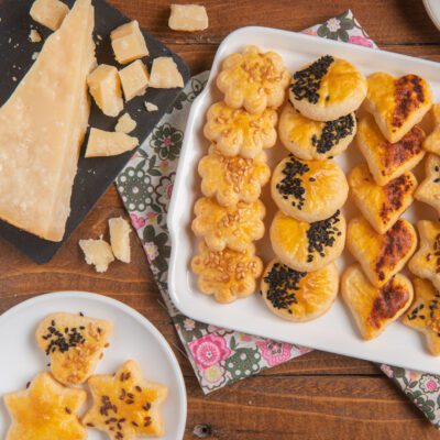 Frollini al parmigiano in varie forme con semi di sesamo, accanto a scaglie di parmigiano
