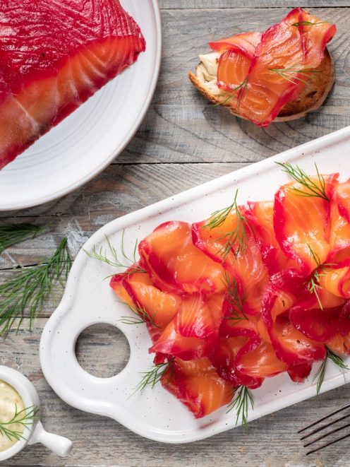 Salmone gravlax affettato sottile con bordi rossi di barbabietola, guarnito con aneto fresco e servito con salsa