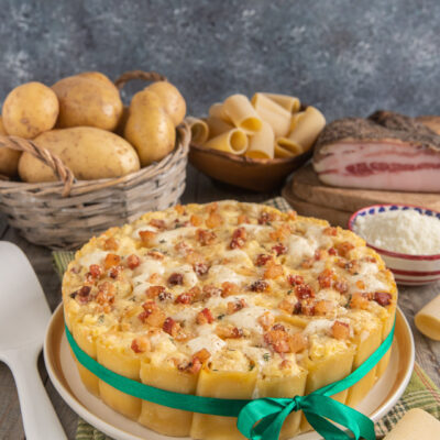 Sformato di paccheri con pancetta a cubetti, mozzarella filante e patate, presentato a torta
