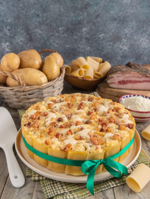 Sformato di paccheri con pancetta a cubetti, mozzarella filante e patate, presentato a torta