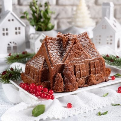 Torta di Natale a forma di casetta spolverata di zucchero a velo, decorata con bacche rosse