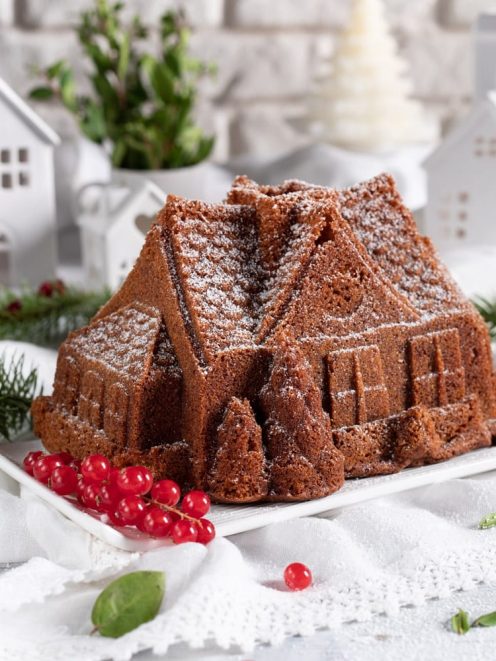 Torta di Natale a forma di casetta spolverata di zucchero a velo, decorata con bacche rosse