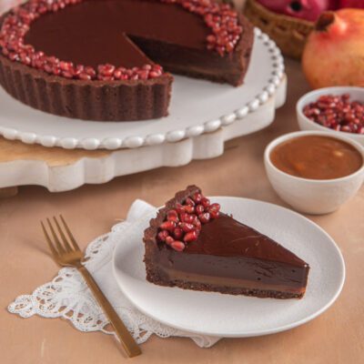 Crostata al cacao con caramello e cioccolato senza glutine, una fetta servita con chicchi di melagrana
