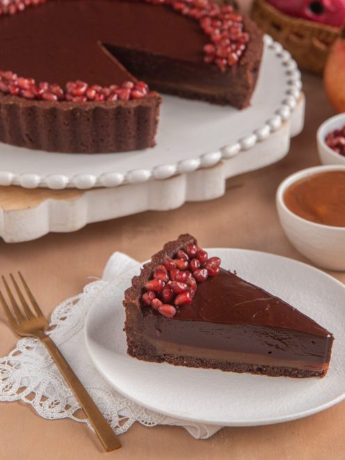 Crostata al cacao con caramello e cioccolato senza glutine, una fetta servita con chicchi di melagrana