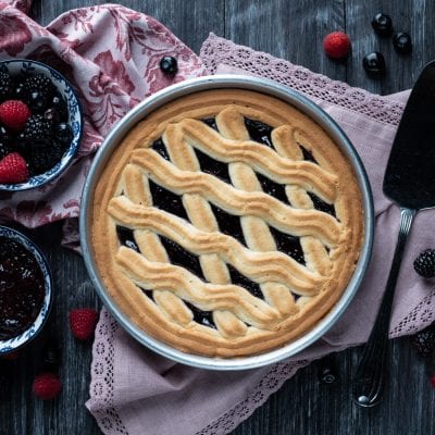 Crostata con frolla montata decorata con strisce ondulate e farcitura di marmellata ai frutti di bosco