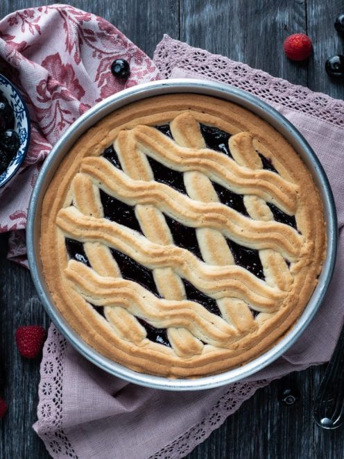 Crostata con frolla montata decorata con strisce ondulate e farcitura di marmellata ai frutti di bosco